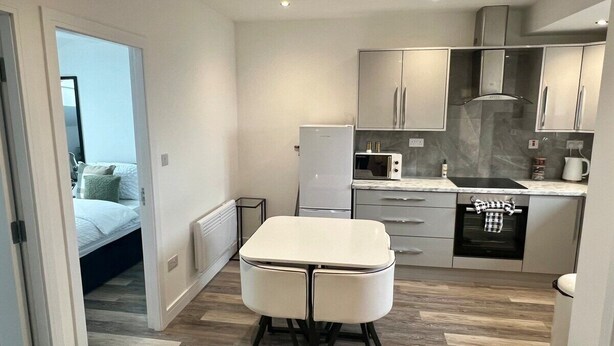 Una cocina compacta con una mesa blanca y muebles, un microondas, un refrigerador y un lavavajillas.
