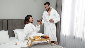 A couple in white robes sitting on a bed with a tray of food and wine glasses. - Hillside Guest House (Yerevan)