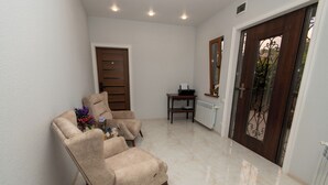 A spacious room with a beige armchair, a small table with a laptop, and a door with a decorative glass panel.