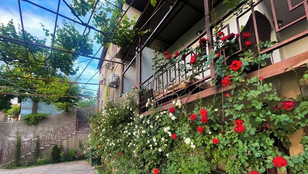 A pathway leading to a building with a balcony adorned with red and white flowers.