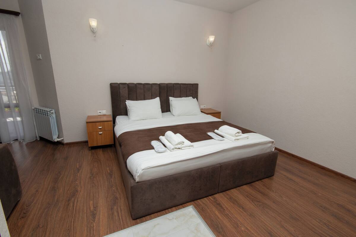 Una habitación de hotel moderna con una cama grande, suelo de madera y dos mesitas de noche.