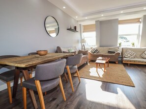 A modern living room with a wooden dining table, grey upholstered chairs, a sofa, and a coffee table. - Priory (St Austell)