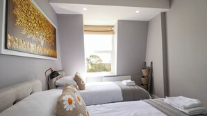 A hotel room with two beds, a large window with a view, a radiator, and a painting on the wall. - Priory (St Austell)