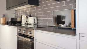 A modern kitchen with stainless steel appliances, a brick backsplash, and a built-in oven. - Priory (St Austell)