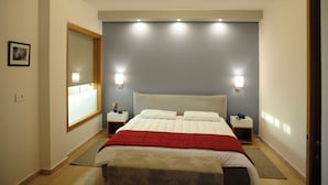 A hotel room with a large bed, two bedside tables, a nightstand, a red throw blanket, and a window with blinds.