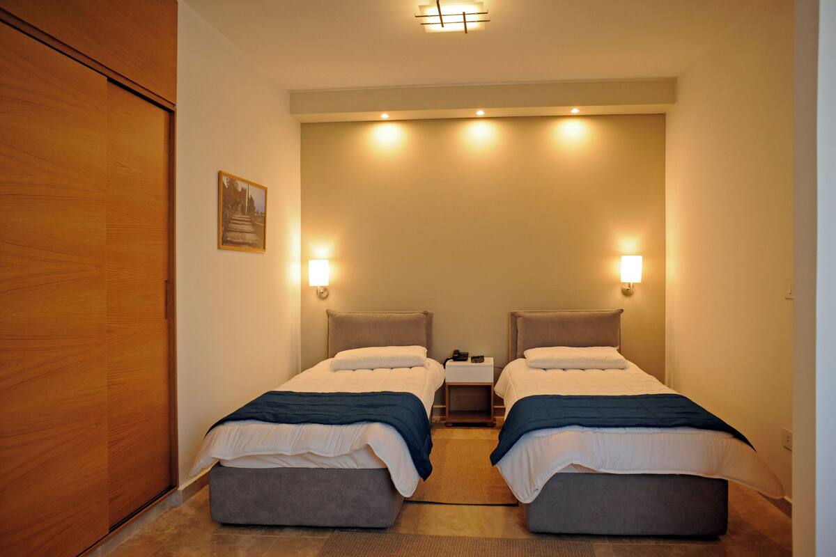 Une chambre d’hôtel avec deux lits, une armoire en bois, une table de chevet et des lampes fixées au mur.