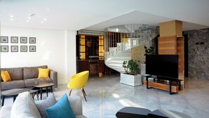 A modern living room with a sofa, chairs, a TV, and a staircase leading to a balcony.