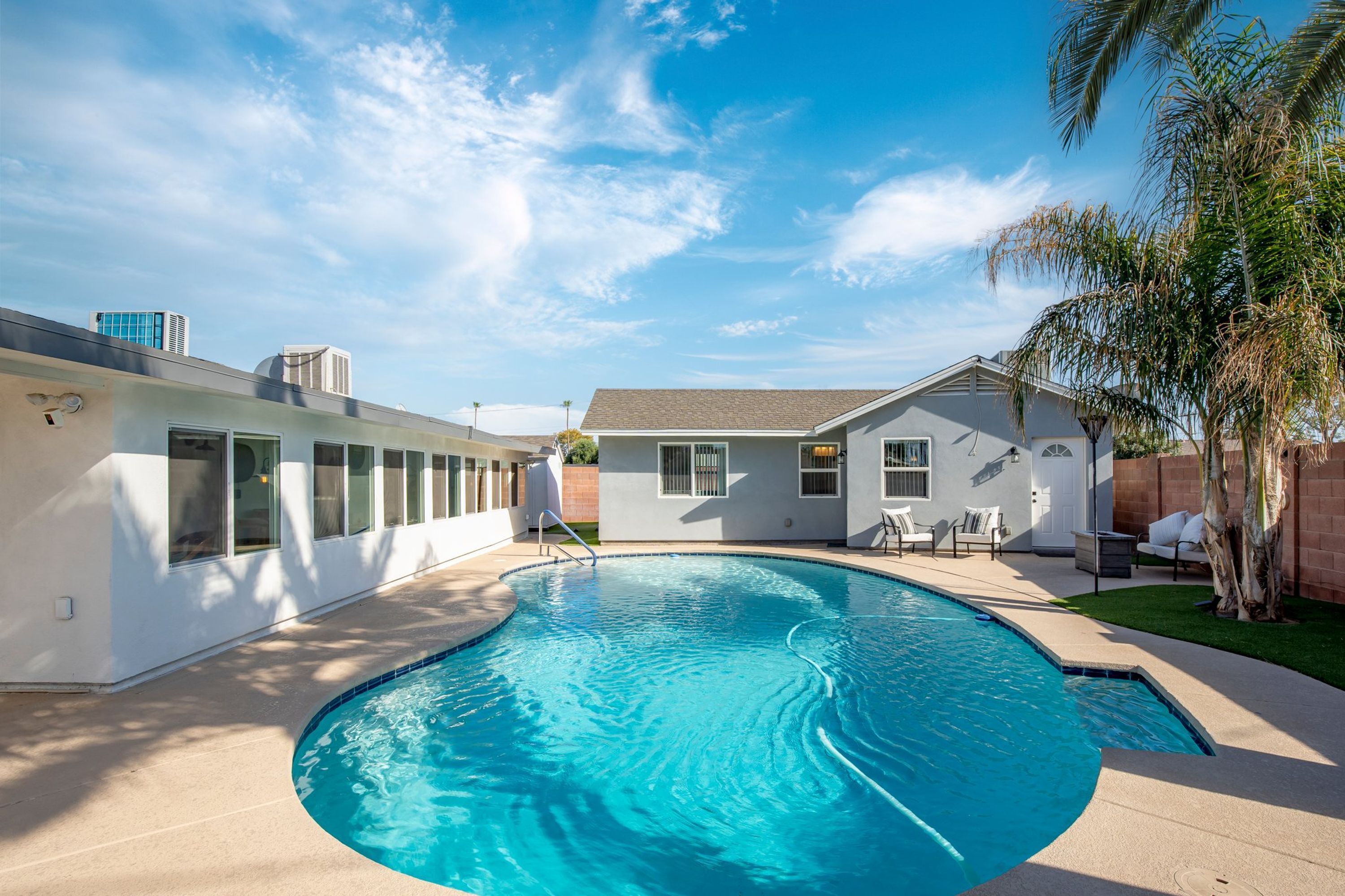 A swimming pool with a curved edge, surrounded by a patio area with chairs and a small house-like structure.
