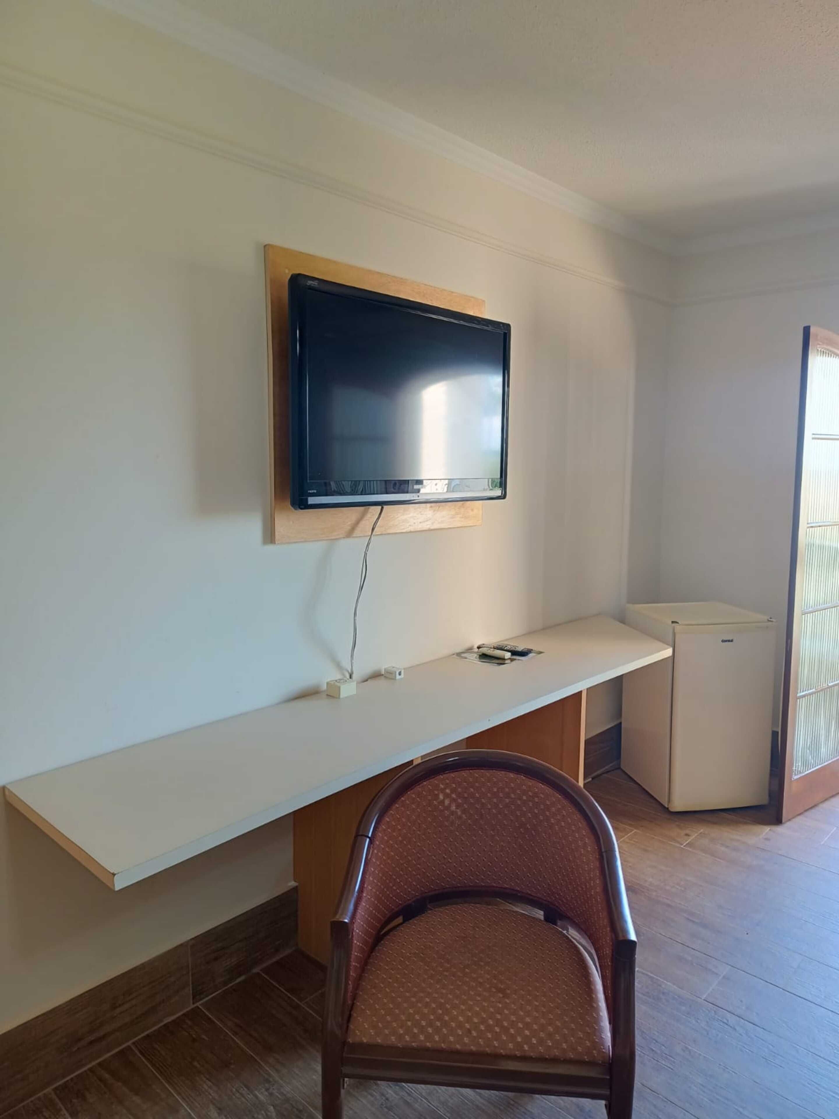 Ein Zimmer mit Flachbildfernseher an der Wand, einer kleinen Küchenzeile und einem Sessel.