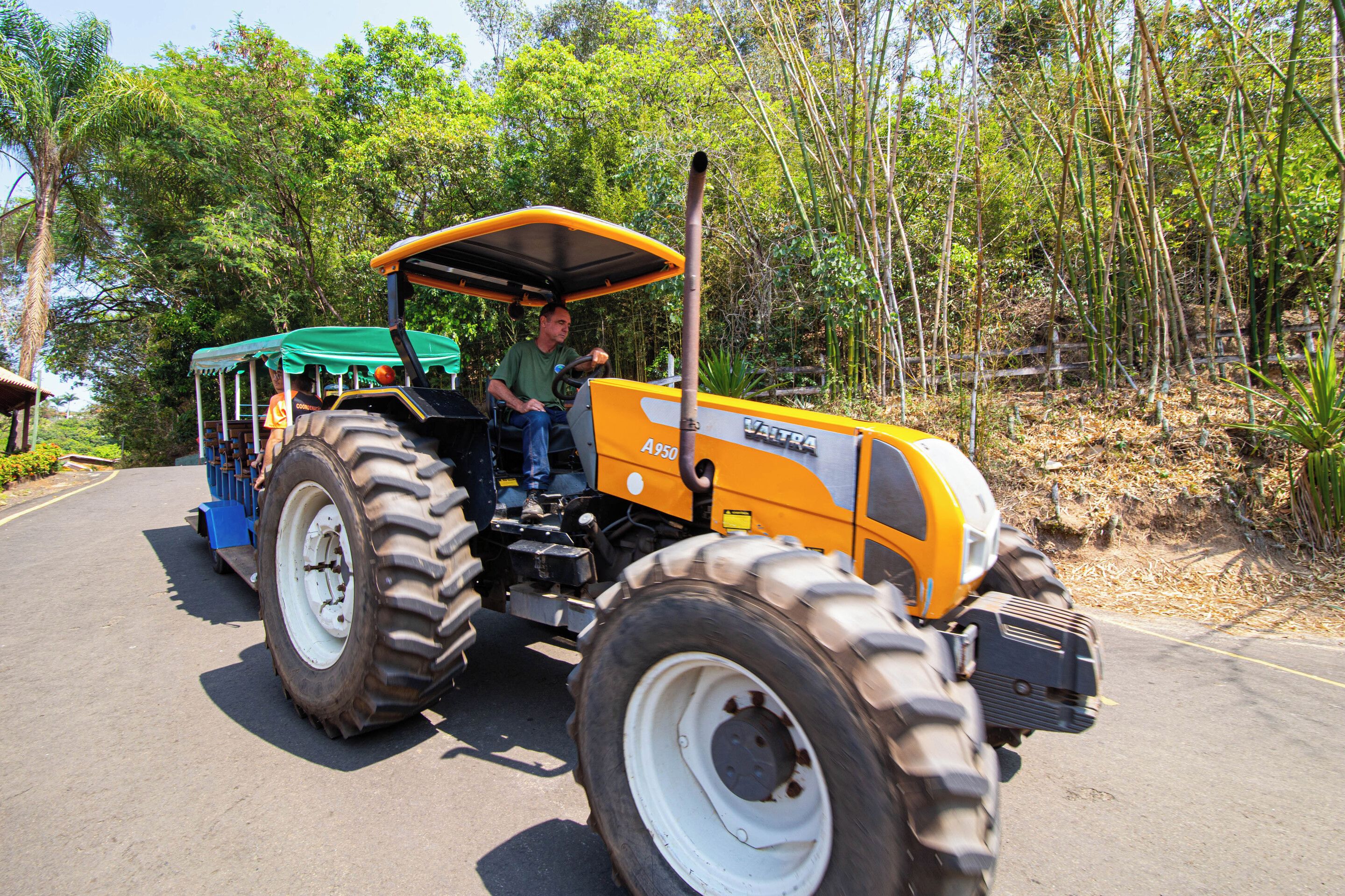 A yellow tractor with a green canopy, parked on a paved road with trees in the background.