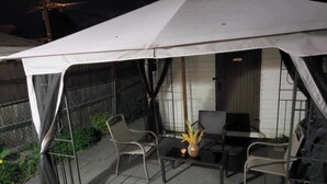 Un patio exterior con una zona de estar techada, que incluye dos sillas y una mesa.