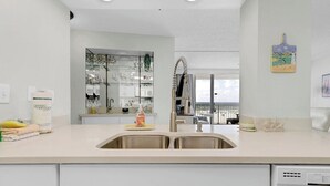 A modern kitchen with a double sink, white cabinetry, and a view of the balcony. - Beach Front 3BR Condo | Gorgeous Views | Whaler 2D (Gulf Shores)