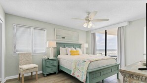 A bedroom with a bed, a chair, a nightstand, a ceiling fan, and a view of the outdoors. - Beach Front 3BR Condo | Gorgeous Views | Whaler 2D (Gulf Shores)