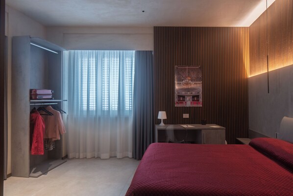 Habitación de hotel con cama, escritorio, silla, armario y ventana con cortinas.