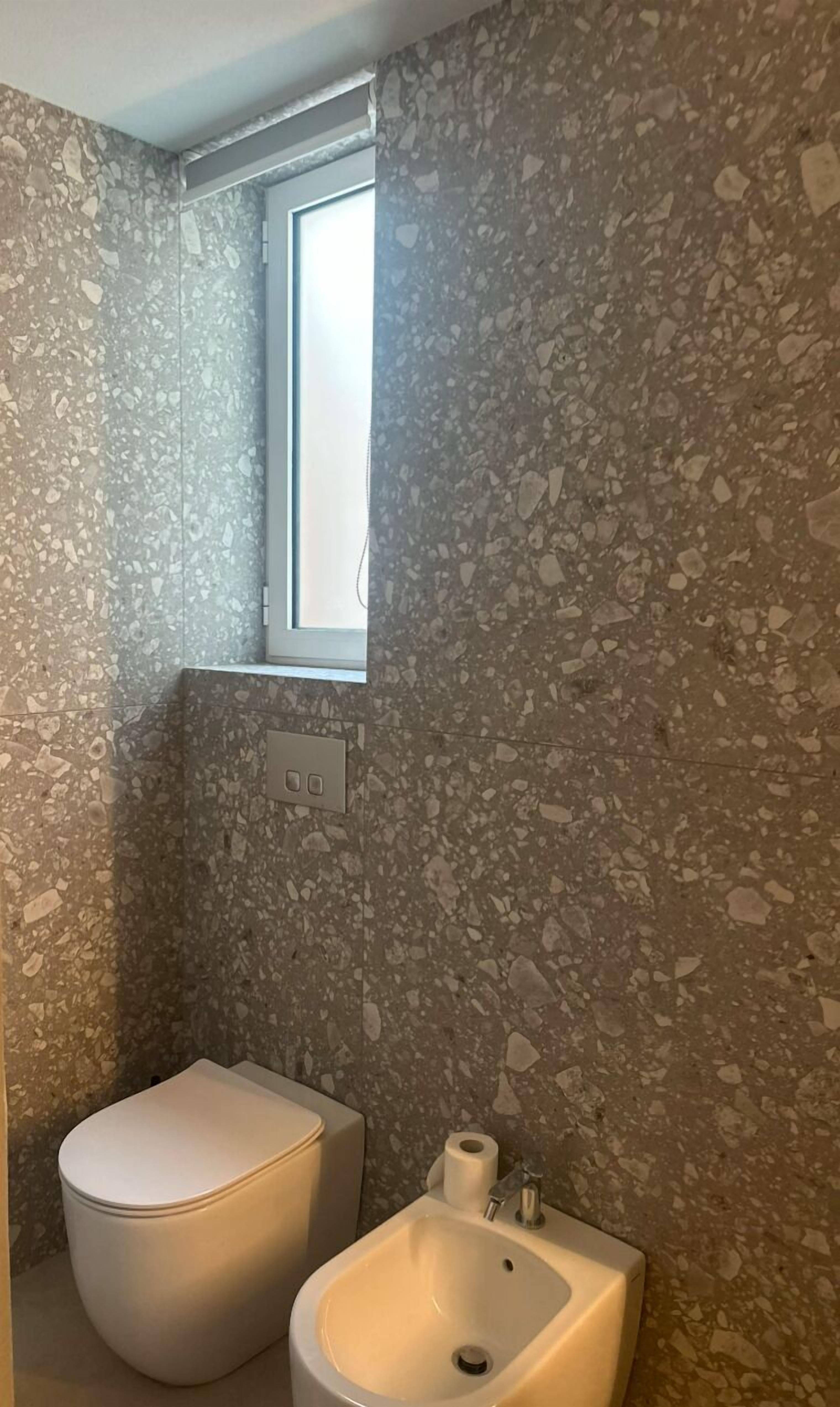 Ein Badezimmer mit Terrazzowand, Toilette, Bidet und Fenster.