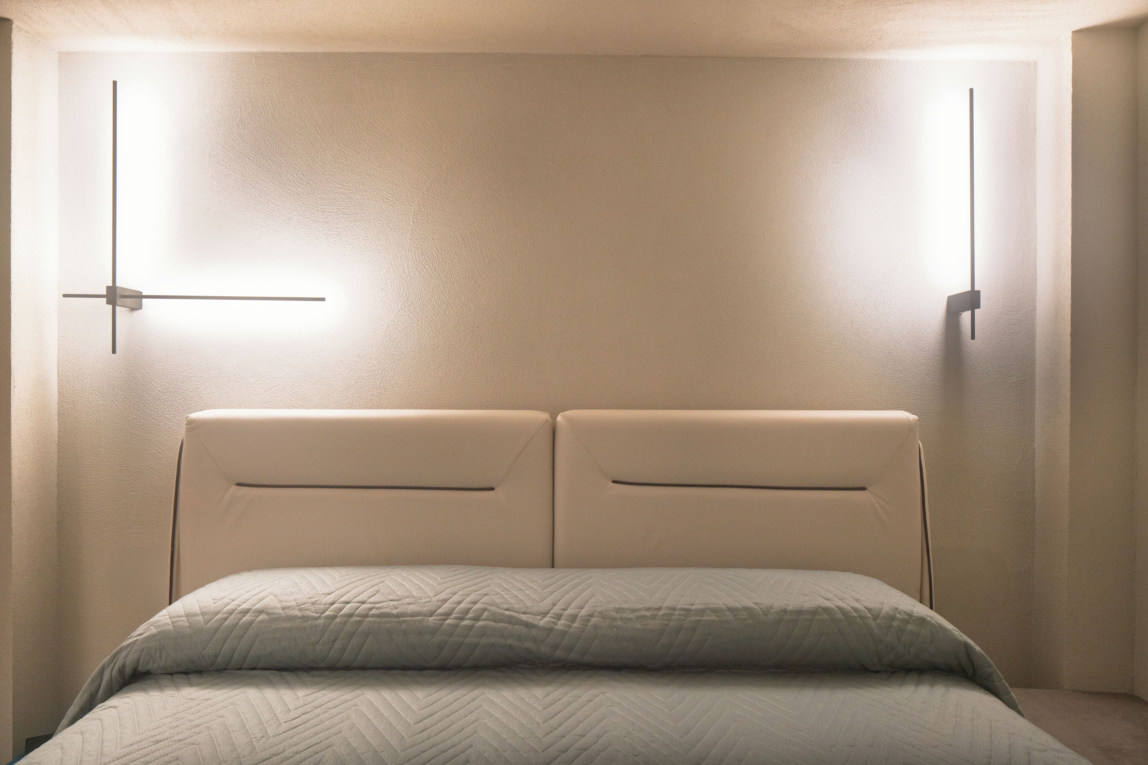 Ein Bett mit einem Bettbezug in Fischgrätmuster und zwei Wandleuchten.
