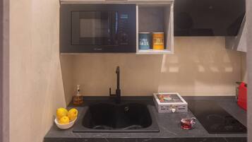 A modern kitchen with a black sink, a microwave, a stove, and a shelf with salt and sugar containers.