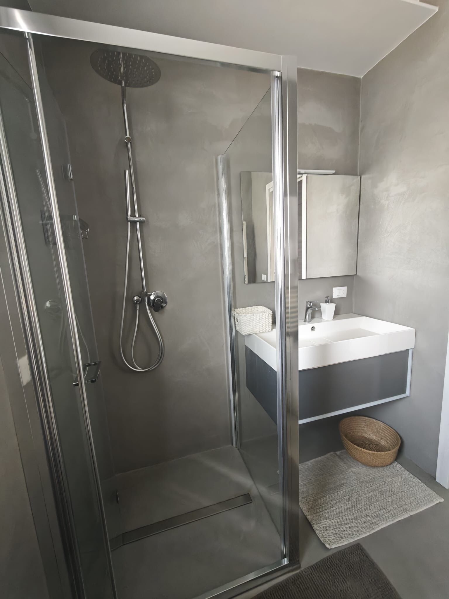 Uma casa de banho moderna com cabine de duche em vidro, lavatório branco e um espelho grande.