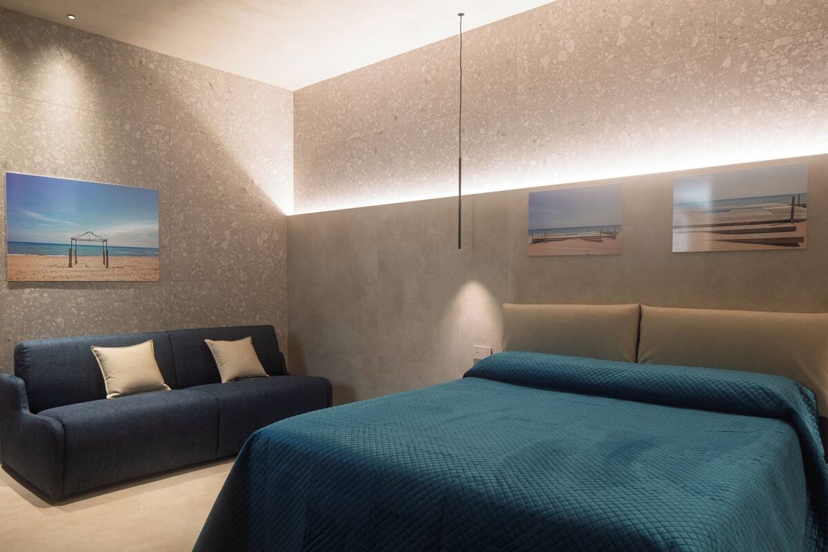 Moderni hotellihuone, jossa on suuri sänky, sohva ja taideteoksia seinillä.