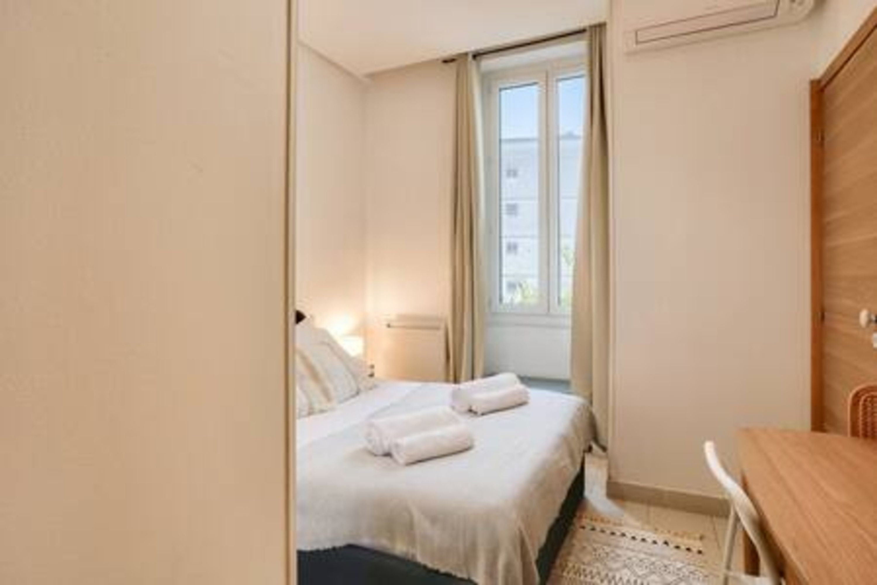 Une chambre d’hôtel avec un lit, un bureau en bois et une fenêtre avec des rideaux.