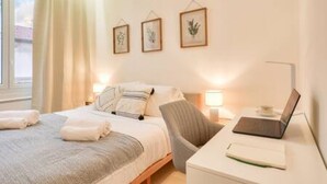 Une chambre d’hôtel avec un lit, un bureau avec un ordinateur portable et trois reproductions botaniques encadrées accrochées au mur.