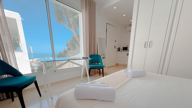 A hotel room with a large bed, a view of the sea, a dining area, and a balcony with a chair. - The Amazing Studio in Site Arch Ologique de Carthage (La Marsa)
