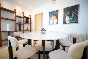 Un comedor moderno con una mesa redonda, seis sillas, estanterías de madera y dos obras de arte colgadas en la pared.