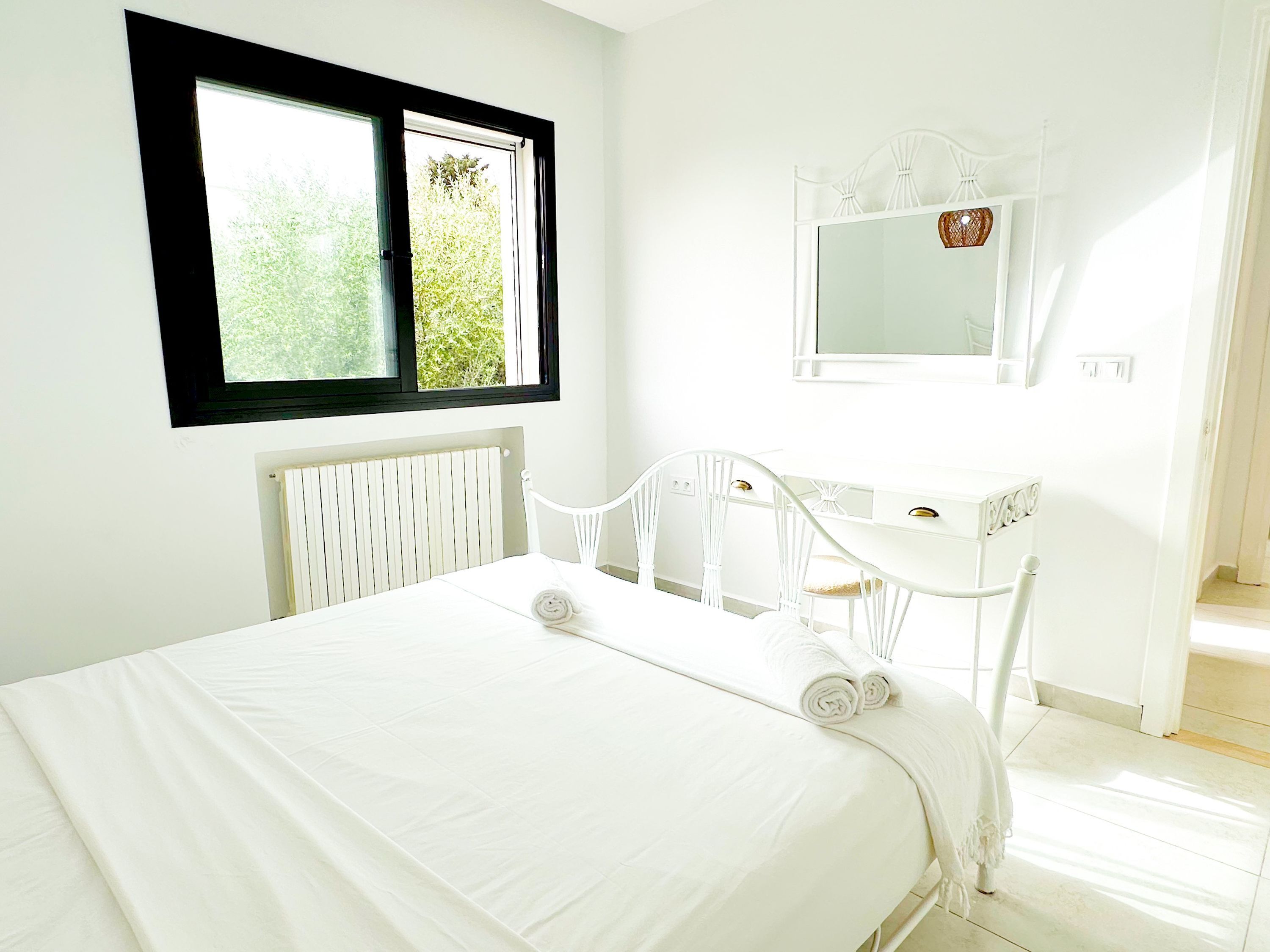 A bedroom with a bed, a white desk, and a mirror.