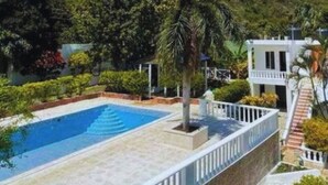 A swimming pool with a white fence, surrounded by lush greenery and a hillside in the background. - Airisha Villa Paradise (Los Patos)
