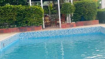Una piscina con borde de azulejos y un pabellón que dice "El Patio de Rubi".
