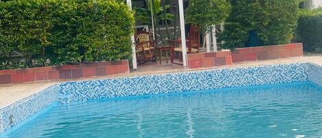 Una piscina con borde de azulejos y un pabellón que dice "El Patio de Rubi".