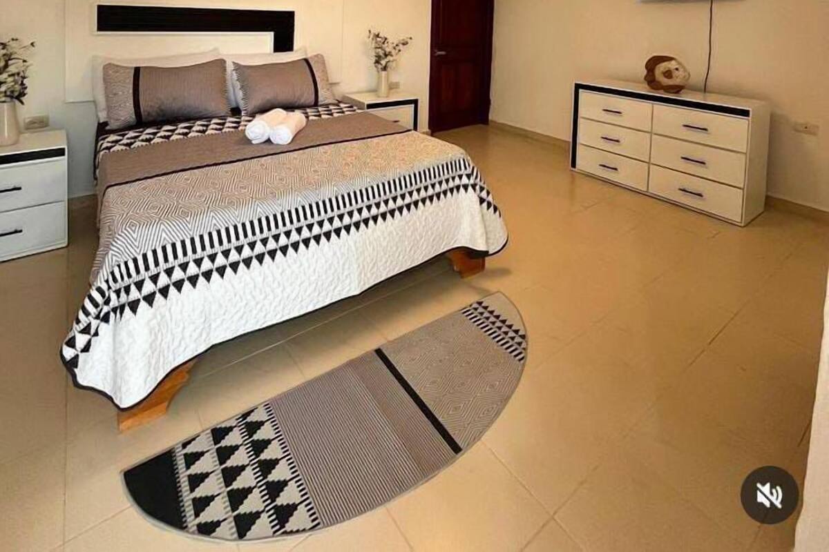 A bedroom with a bed, a nightstand, a dresser, a television, and a ceiling light.