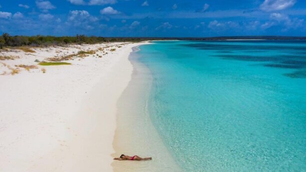 A beach with clear turquoise waters and a person lying on the sand. - Airisha Villa Paradise (Los Patos)