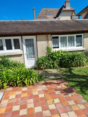 A house with a tiled patio, a door, and windows with lace curtains. - House located 100 meters from the ocean. (Luc-sur-Mer)