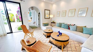 A modern living room with wicker furniture, a white sofa, and a colorful rug. - Villa Azur Piscine Bord de mer a Hammamet (Hammamet)