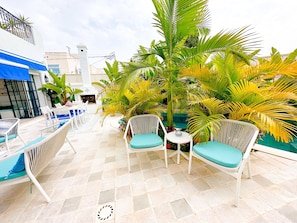 A patio area with white wicker chairs and a table, surrounded by lush tropical plants. - Villa Azur Piscine Bord de mer a Hammamet (Hammamet)