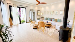 A modern living room with a sofa, two wicker chairs, a round table, a black wood stove, and a ceiling fan. - Villa Azur Piscine Bord de mer a Hammamet (Hammamet)