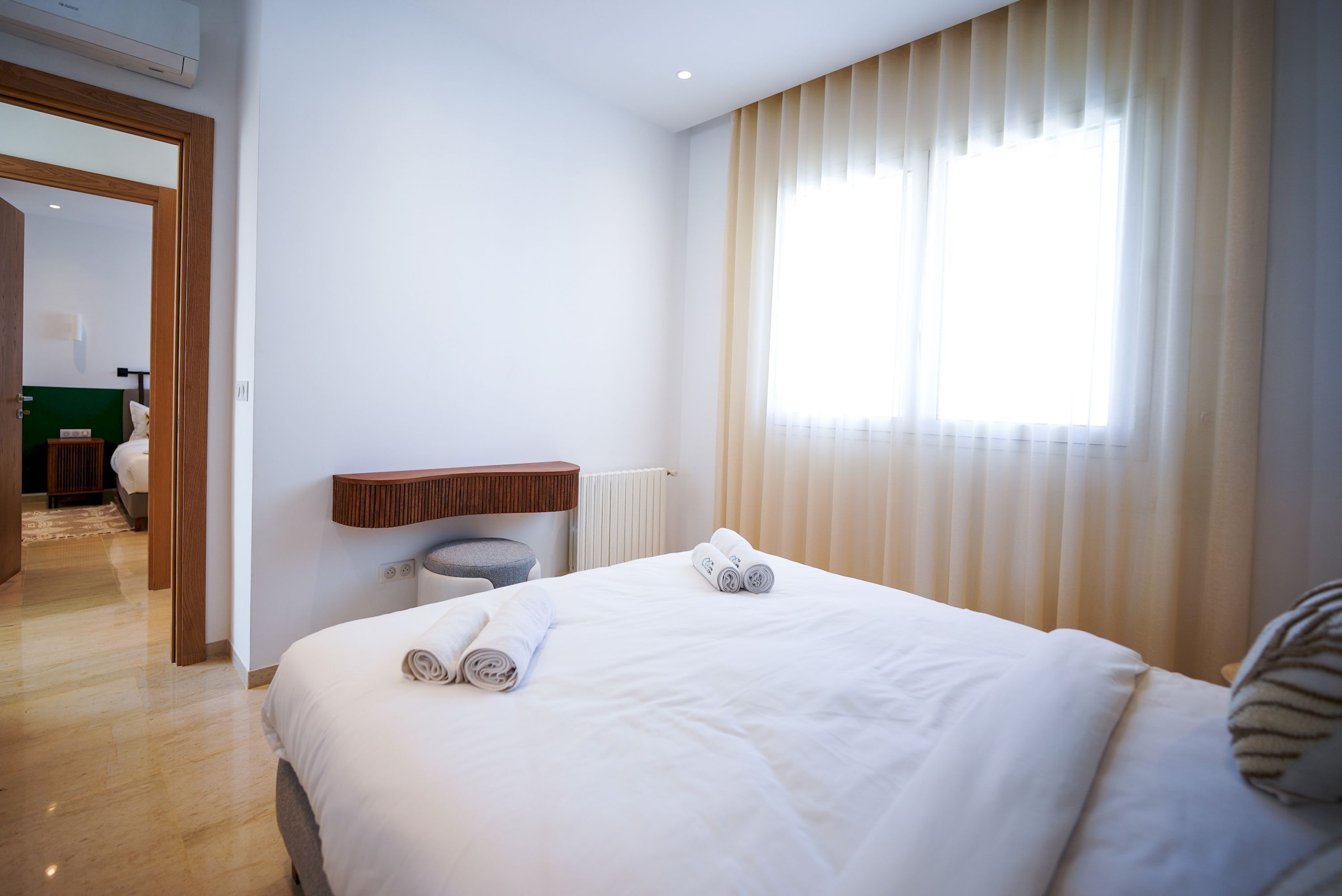 A hotel room with a large bed, a wooden headboard, a small bedside table, and a window with blinds.