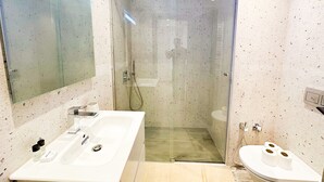 Ein modernes Badezimmer mit einer einteiligen Duschkabine, einem weißen Waschbecken mit Pflegeprodukten und einer Toilette mit Toilettenpapier.