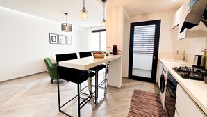 Eine moderne Küche mit Essbereich, ausgestattet mit einer weißen Arbeitsplatte, schwarzen Stühlen und Holzboden.