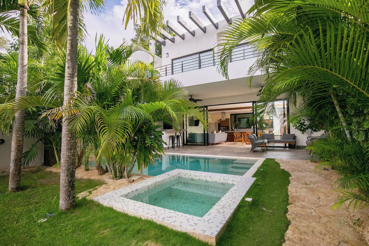A modern house with a swimming pool, surrounded by lush greenery and palm trees.