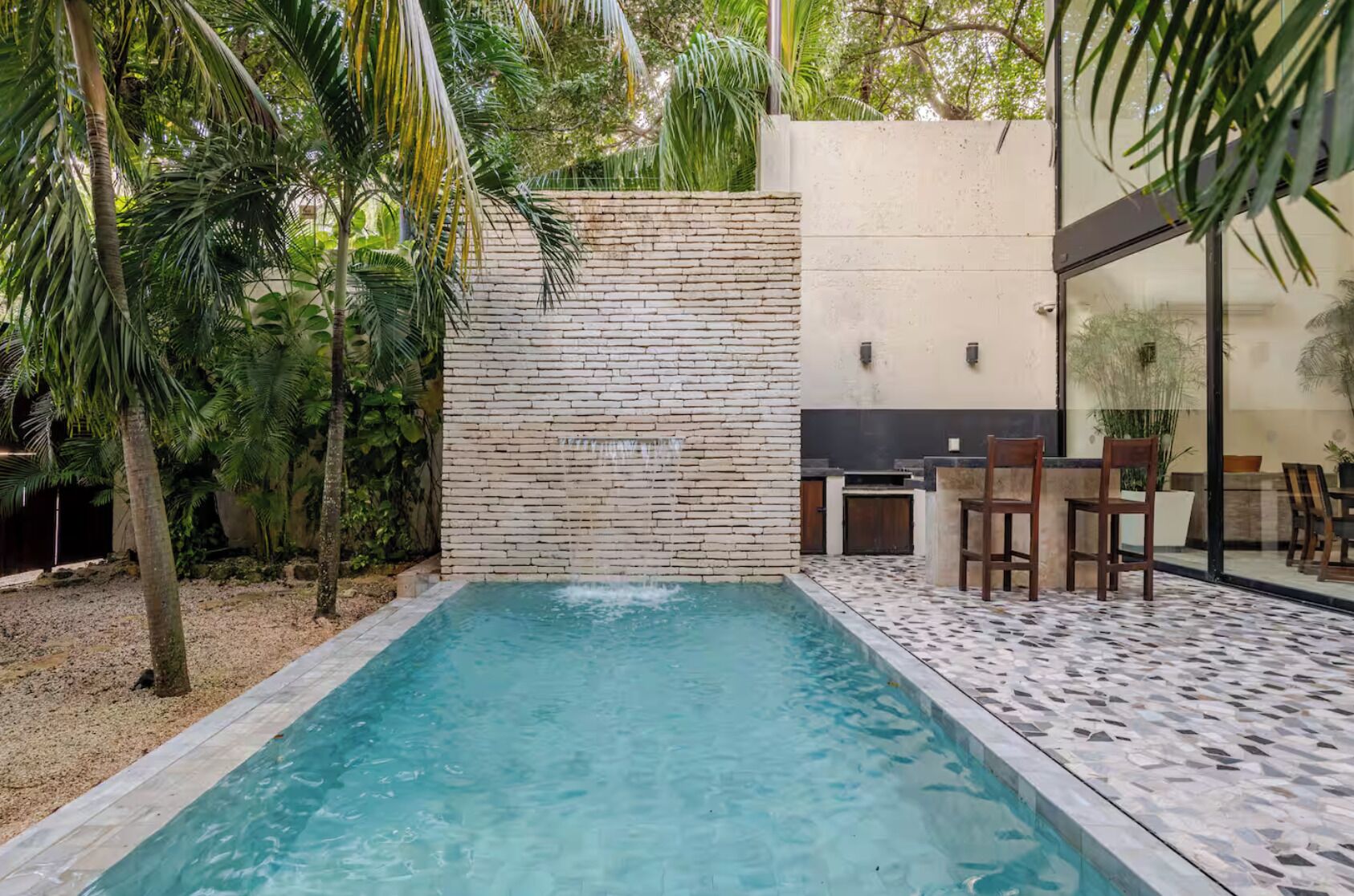 A swimming pool with a stone wall and tropical plants.