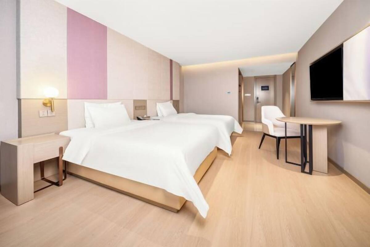 A hotel room with a bed, bedside tables, a desk, a chair, and a TV.