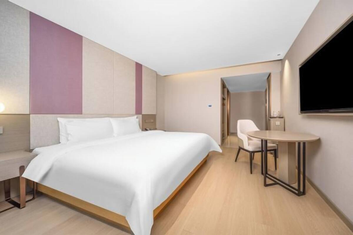 A modern hotel room with a bed, a desk, a chair, a TV, and a small table.