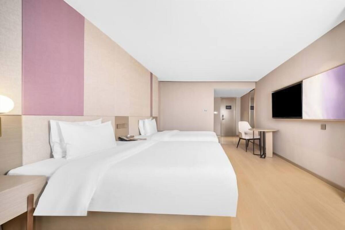 A hotel room with a bed, bedside table, chair, TV, and a small table with a chair.