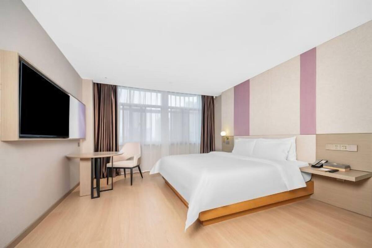 A hotel room with a bed, a desk, a chair, a TV, and a window with curtains.