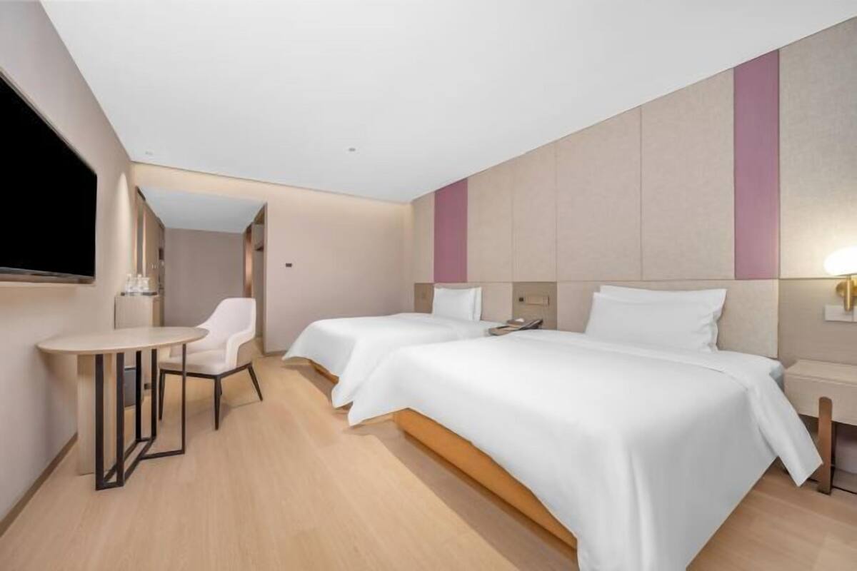 A hotel room with two beds, a small table, a chair, and a TV.