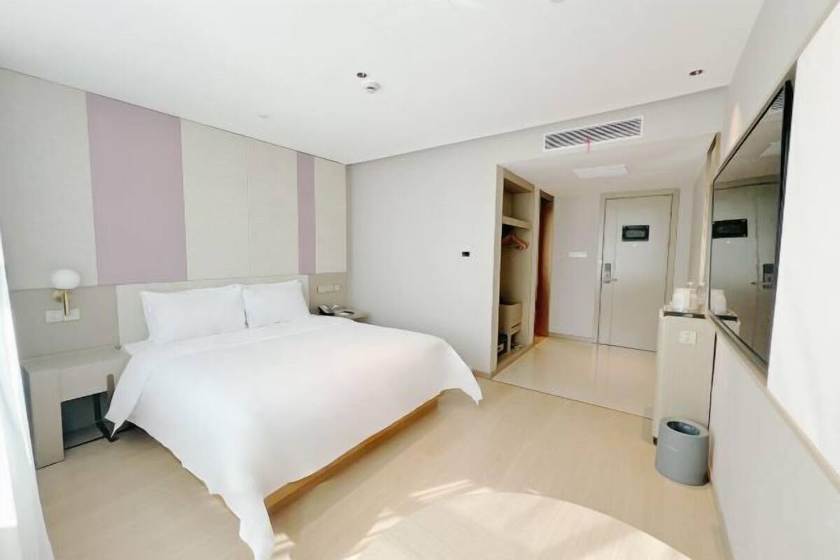 A modern hotel room with a large bed, a bedside table, a mirror, and a wardrobe.