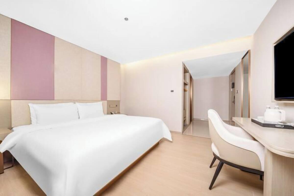 A modern hotel room with a large bed, a desk, and a television.