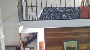 Une pièce avec un lit superposé, un escalier en bois, un lit recouvert d’une courtepointe à motifs floraux, une chaise et un tableau encadré accroché au mur.
